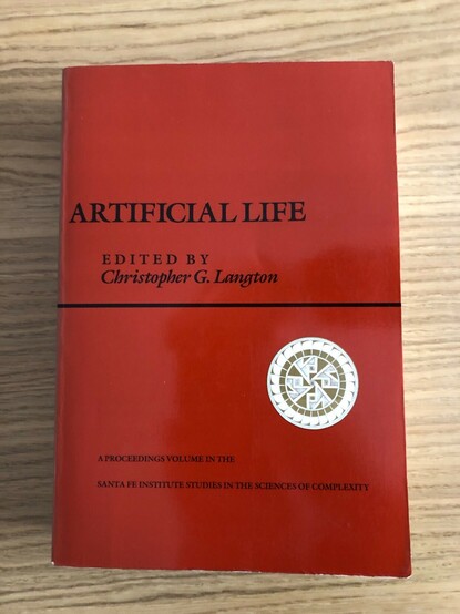 Book on desk: "Artificial Life" edited by Christopher Langton. Proceedings of a workshop held at the Santa Fe Institute where the term "Artificial Life" was first coined.