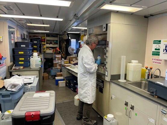 Scientist in a lab coat working in a fume hood on a research ship.