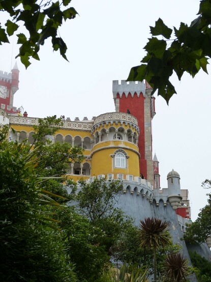 A romanticist palace, with grey walls and yellow and red structures projecting above the walls.