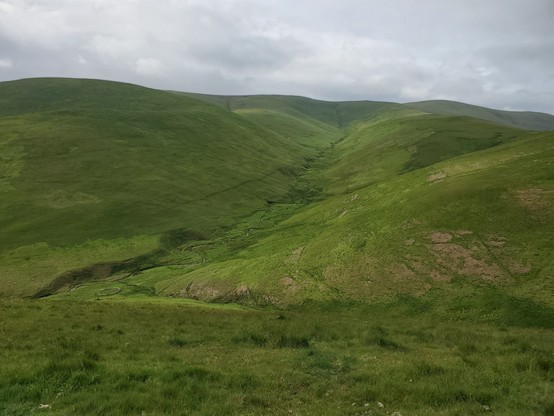 A very green view looking down steep slopes across to a stream draining hills in the distance.

The foreground here is the site of the crash of the DORNIER 217 U5+DL German Aircraft which crashed here on 15th March 1943