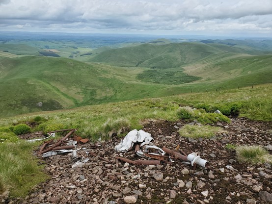 Some twisted metal and rusting pipe lie in a small area of bare, rocky ground  on a grassy slope. Away to the north under a cloudy sky, green hills stretch down to Scottish Border's countryside to the horizon.

This is the remains of a De Havilland Mosquito, which crashed on 12 December 1944, killing pilot Henry Medcalf (27) and navigator Ronald Bellamy (21)