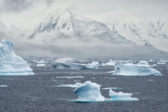 image/jpeg scattered icebergs float in the ocean against a background of snow covered mountainous terrain. Antarctica,  Christopher Michel CCA 2.0.