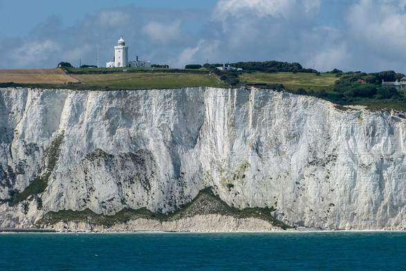 image/jpeg a photo of tall, very white cliffs emerging from blue water. The cliff tops are covered in a thin layer of green grass, and a lighthouse is seen in the distance. Photo from Archangel12 CC-BY-SA 2.0.